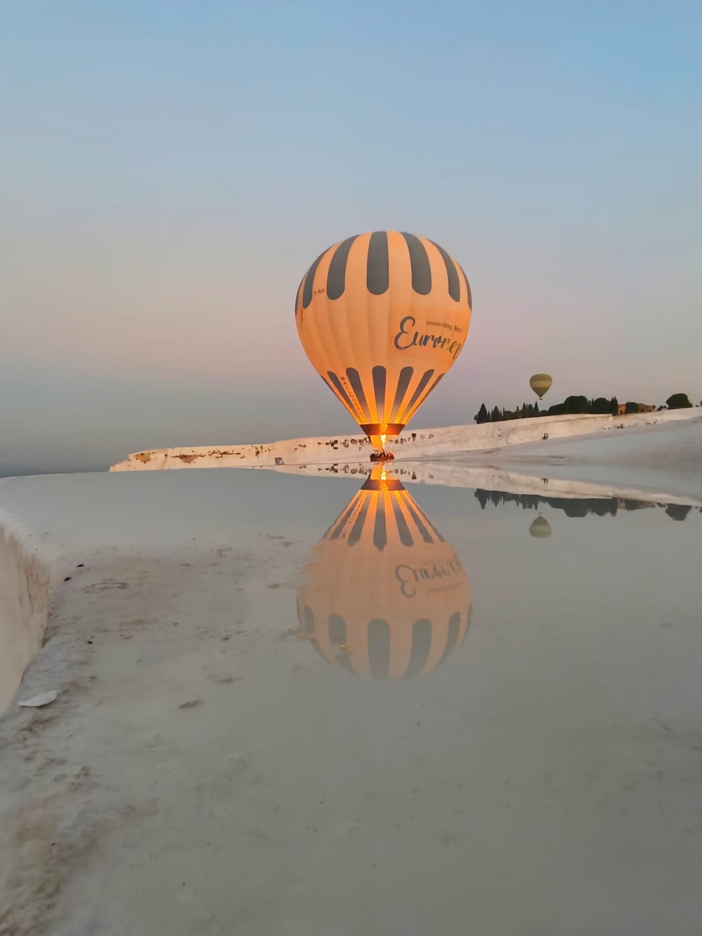 Glowing hot air balloon reflected in Pamukkale terrace pool at golden hour