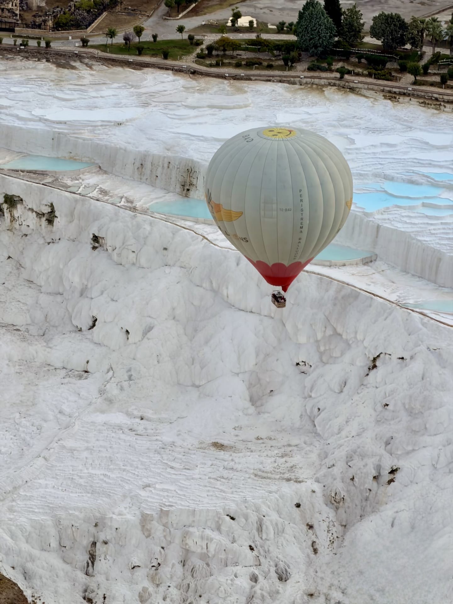 Hot air balloon floating above Pamukkale turquoise thermal pools