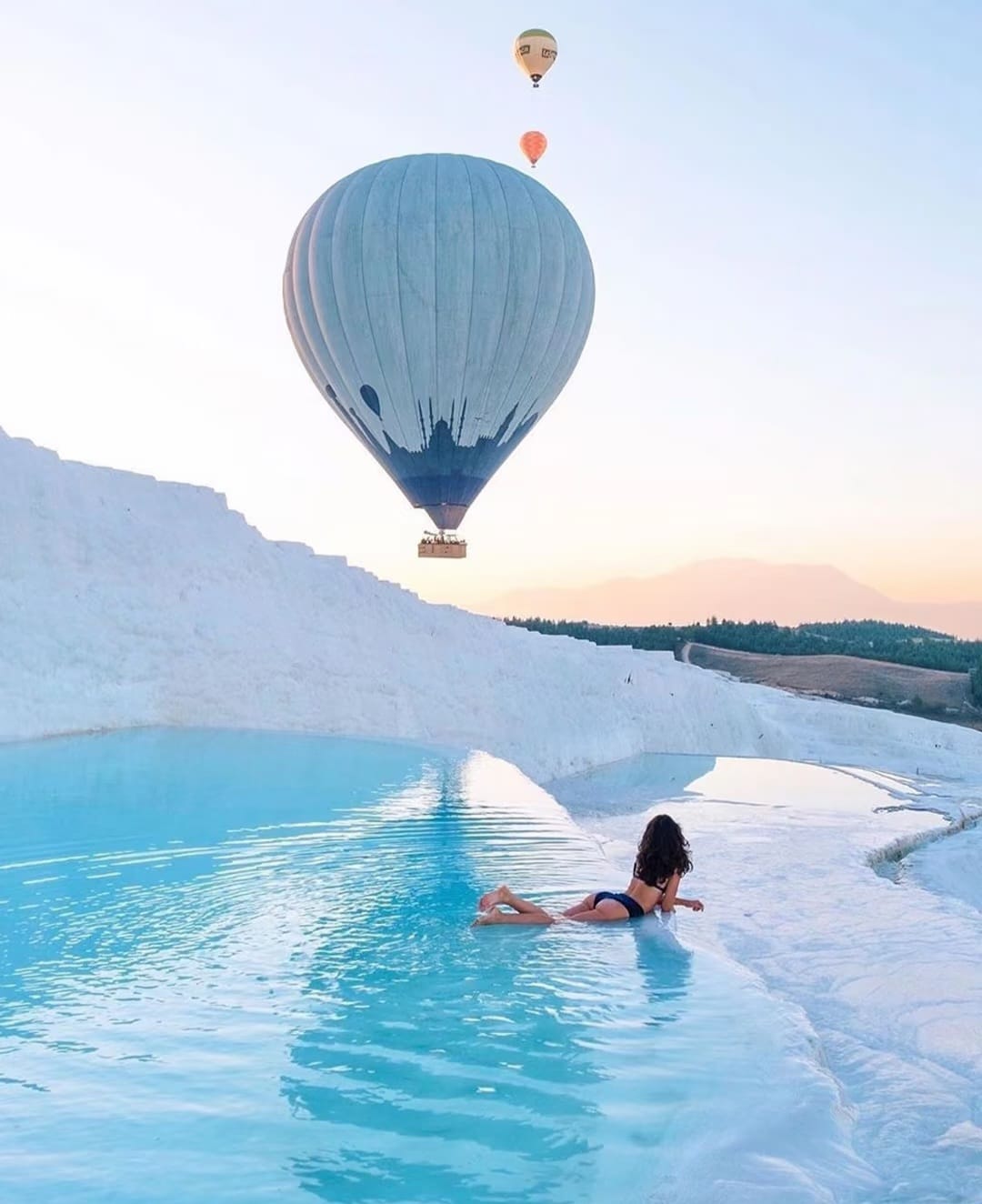 Sunrise view of Pamukkale pools with hot air balloons in the sky